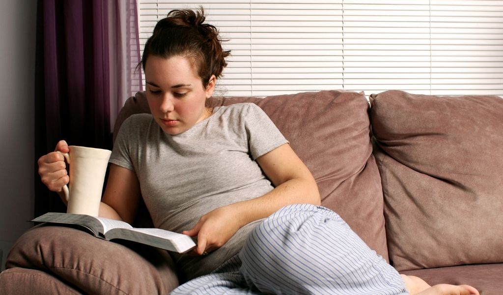 women on couch reading the bible and drinking tea
