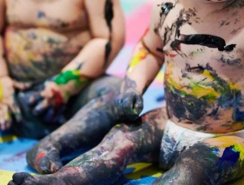 two babies sitting in the floor with paint all over them.