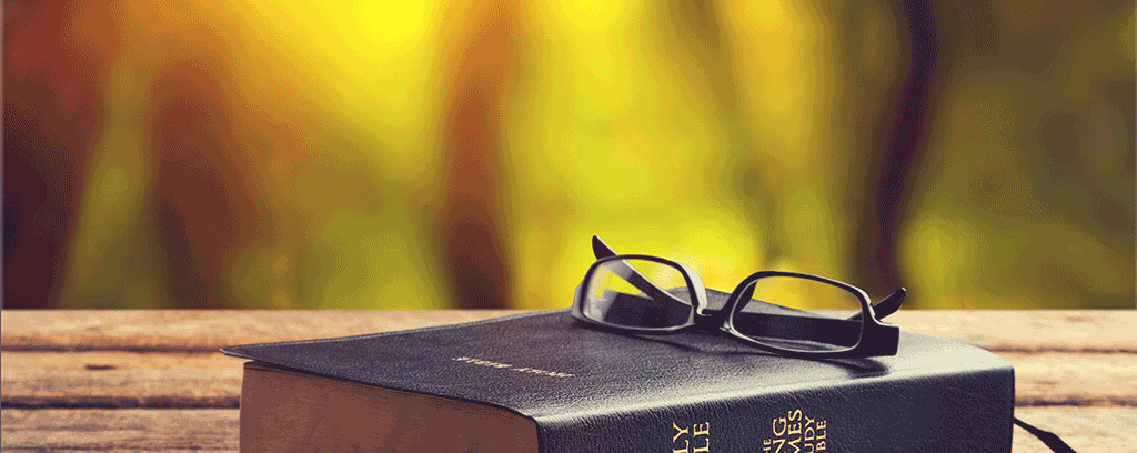 Bible sitting on a wooden table with a pair of glasses setting on top of bible